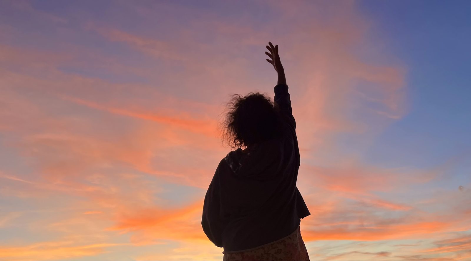 Silhouette of a person with arms raised against a vivid Paros sunset
