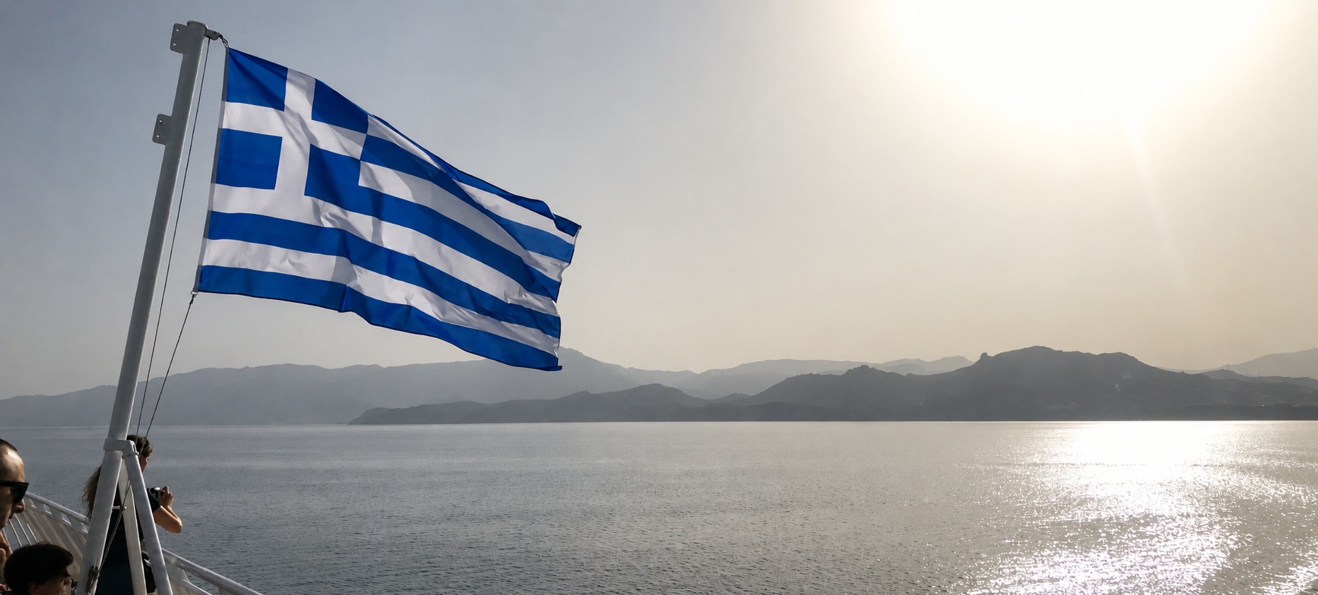 Greek flag flying from a ferry, sailing toward the islands
